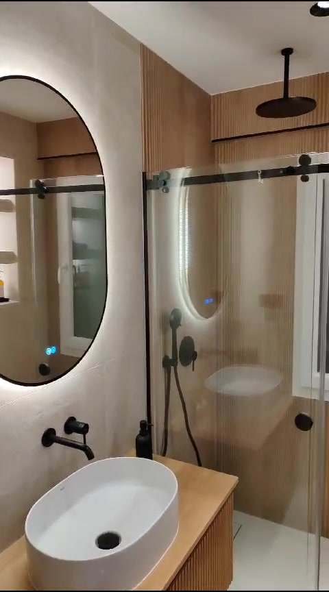 Baño terminado con lavabo ovalado, espejo con luz y ducha con mampara negra